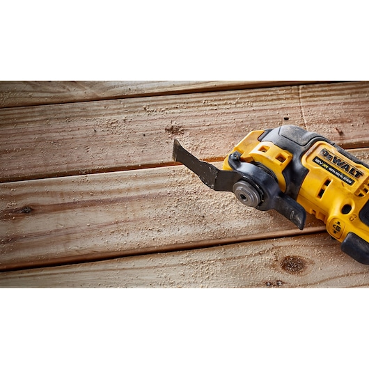 DEWALT cordless oscillating tool cutting wooden planks, sawdust scattered on surface.
