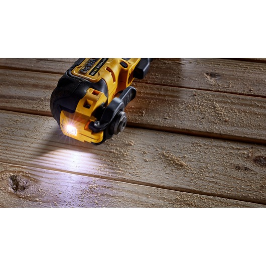 DEWALT power tool with LED light, cutting wooden boards, sawdust visible on the surface.