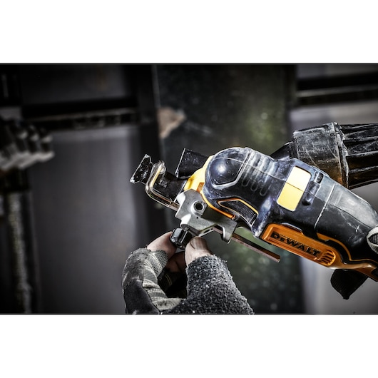 A close-up image showing a DEWALT cordless oscillating multi-tool being operated by a person wearing work gloves. The tool is in use, with visible dust and debris on both the tool and gloves.