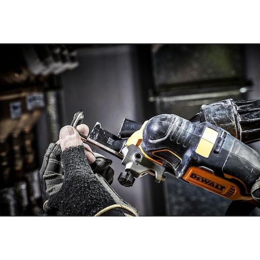Close-up of a gloved hand holding a DEWALT oscillating multi-tool, with a metal blade attachment being adjusted.