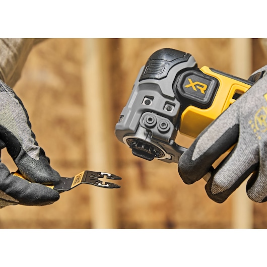 Gloved hands holding a DEWALT XR oscillating tool and blade, ready for attachment during construction work.