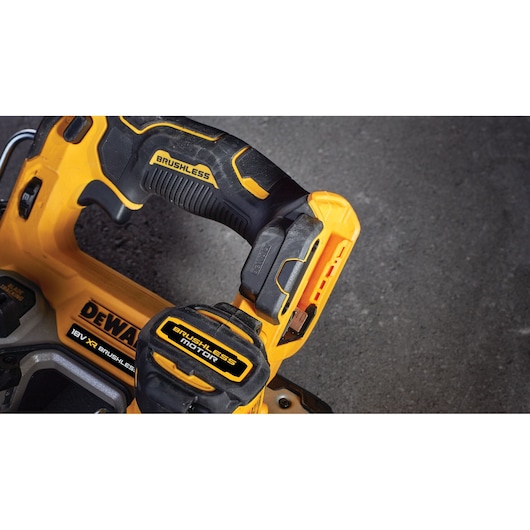 Close-up view of a DEWALT cordless power tool with yellow and black brushless motor details, showing part of the handle and battery pack against a dark surface.