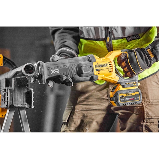 A DEWALT XR cordless reciprocating saw is being used to cut through a pipe in a workshop setting.