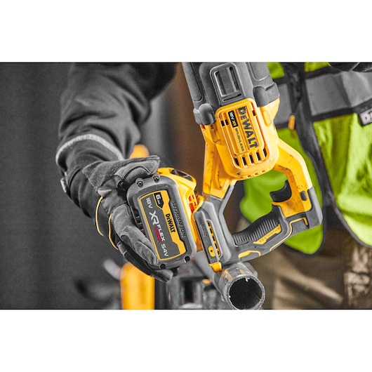Worker uses a DEWALT cordless reciprocating saw to cut a metal pipe. Close-up of tool and gloved hand.