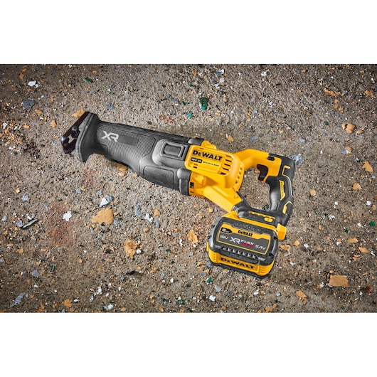 A DEWALT cordless reciprocating saw with black and yellow design, shown resting on a rough, debris-covered surface. The saw features an XR FLEXVOLT lithium-ion battery attached.