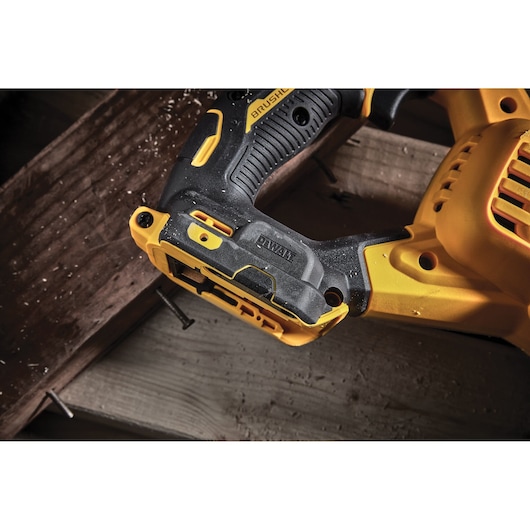 Close-up of a DEWALT cordless reciprocating saw cutting a wooden plank with nails and sawdust.