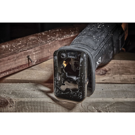Close-up of DEWALT DCS386NT reciprocating saw on wood, covered with dust and wood shavings.