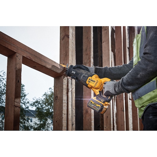 Person uses a DEWALT cordless reciprocating saw to cut wood beams at a construction site.