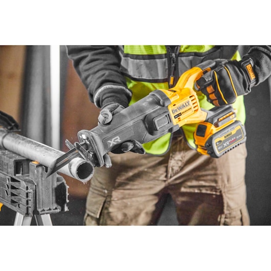 Worker uses a DEWALT cordless reciprocating saw to cut a metal pipe indoors.