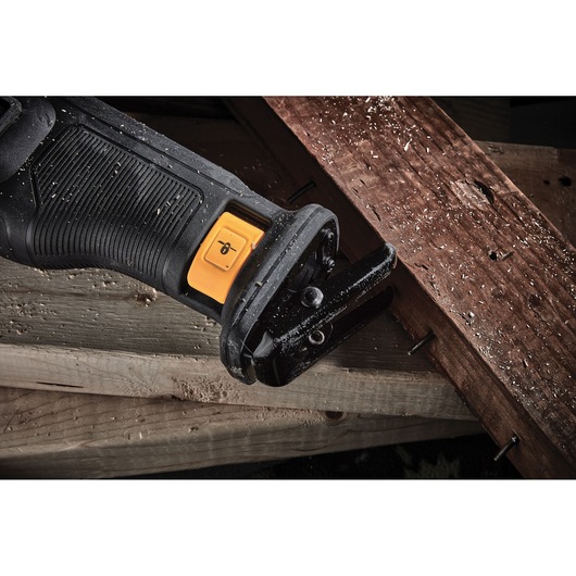 Close-up of a DEWALT power tool cutting through a wooden plank with nails and sawdust visible.