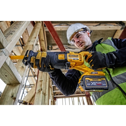 Worker using a DEWALT DCS389N cordless reciprocating saw on wood at a construction site.