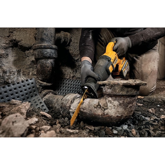 DEWALT cordless saw cutting an old metal pipe in a rugged, dirty environment.