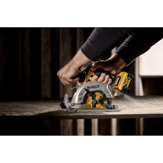 Hands using a DEWALT cordless circular saw to cut wood, with sawdust flying during operation.