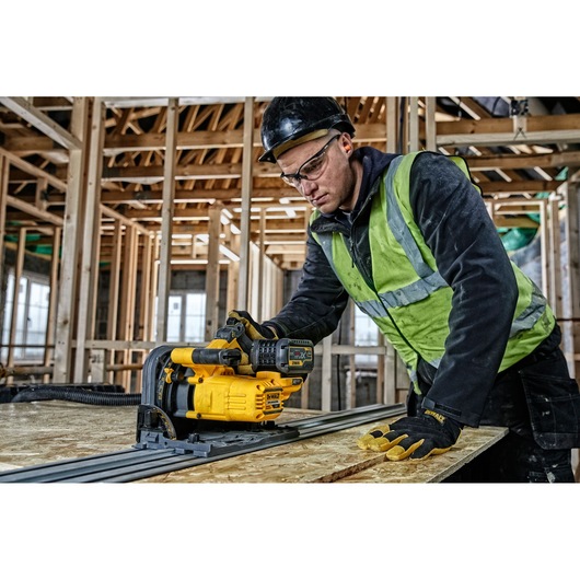 Worker uses a DEWALT DCS520NT power tool to cut wood at a construction site with unfinished framing.