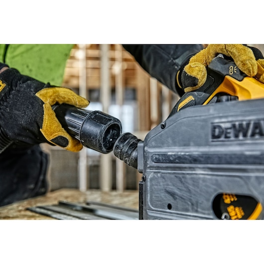 Close-up of a person wearing yellow and black gloves connecting a hose to a DEWALT power tool, with a construction site in