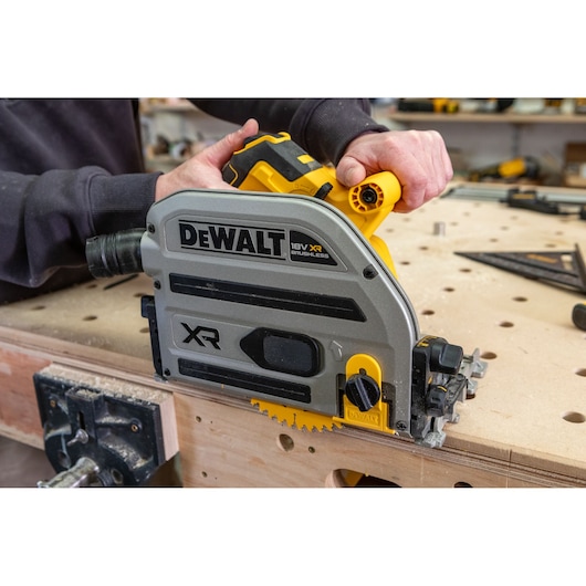 DEWALT DCS525 cordless track saw in use cutting wood on a workbench in a workshop environment.