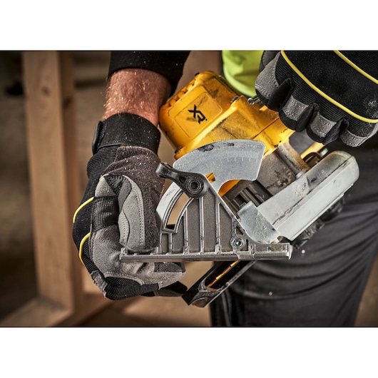 Gloved hands adjust a yellow DEWALT cordless circular saw. Close-up of tool during woodworking.