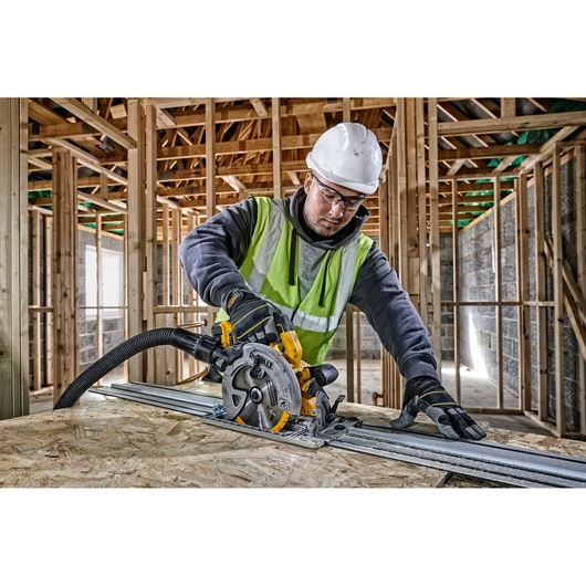 A construction worker wearing a safety helmet and high-visibility vest uses a DEWALT DCS572P2 circular saw to cut wood