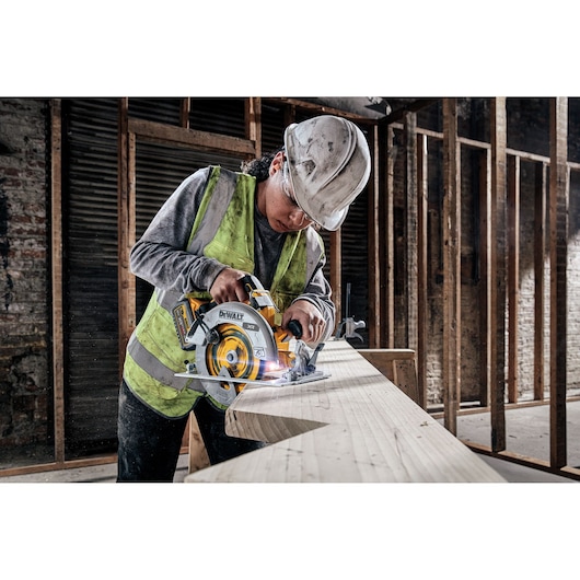 Worker uses DEWALT circular saw to cut wood at a construction site. Safety vest and helmet are worn.