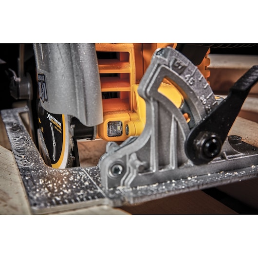 Close-up of a DEWALT DCS573NT circular saw cutting wood, showing adjustment scale and blade guard.