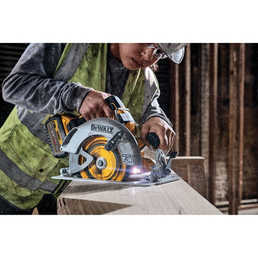 Worker uses a DEWALT cordless circular saw to cut wood on a construction site.