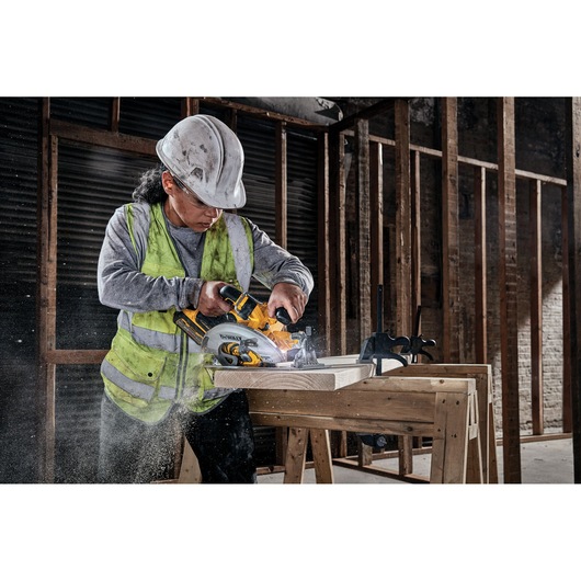 Construction worker using a DEWALT circular saw to cut wood on a workbench in an unfinished building.