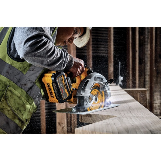 Worker uses a DEWALT cordless circular saw to cut wood on a construction site.