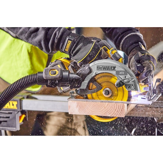 DEWALT circular saw cutting wood, operated by a worker wearing gloves. Sawdust and wood chips are visible.