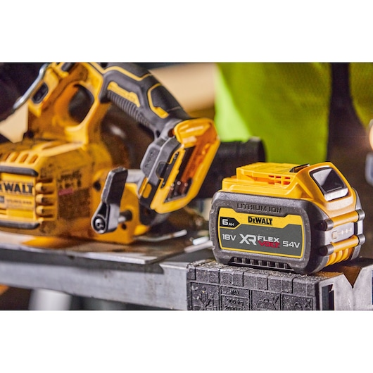DEWALT cordless saw with XR FLEXVOLT 18V/54V battery shown on a metal workbench in a workshop setting.