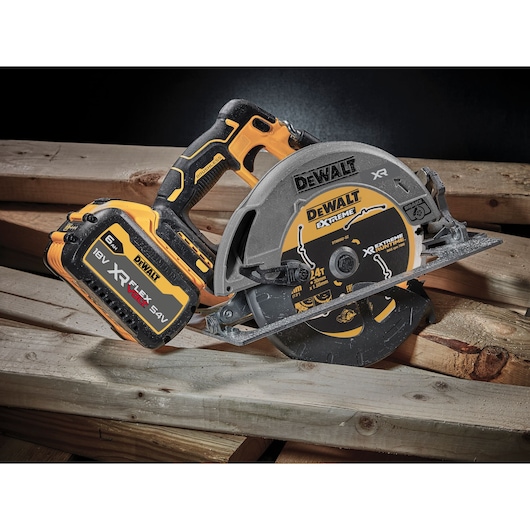 A DEWALT cordless circular saw with an 18V XR FLEXVOLT 6.0Ah battery, placed on stacked wooden planks. The tool is black and yellow, and the saw blade is marked with 'DEWALT EXTREME' and technical details.