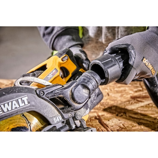 Close-up of a DEWALT XR Flexvolt 54V cordless circular saw with an attachment being connected, held by a person wearing