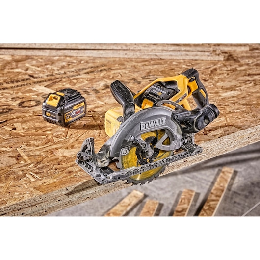 A DEWALT cordless circular saw and a DEWALT XR FLEXVOLT battery placed on a sheet of plywood in a workshop.