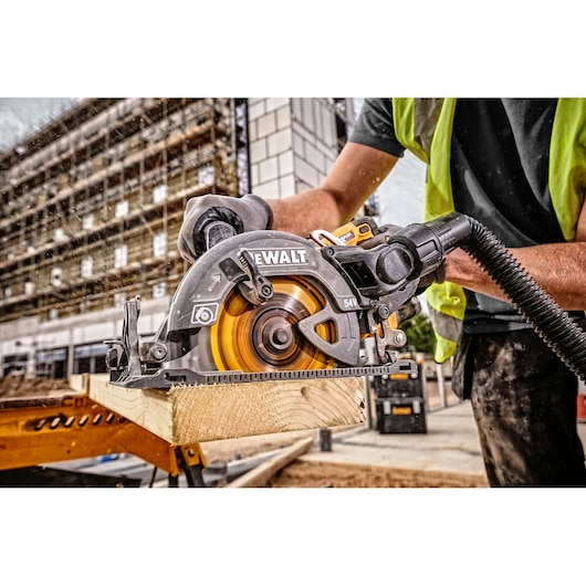 A DEWALT cordless circular saw (model DCS577T2) is being used by a construction worker wearing a safety vest and gloves to