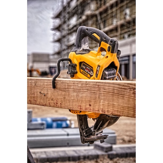 A DEWALT cordless circular saw (model DCS577T2) is shown resting on a wooden beam at a construction site, with scaffolding