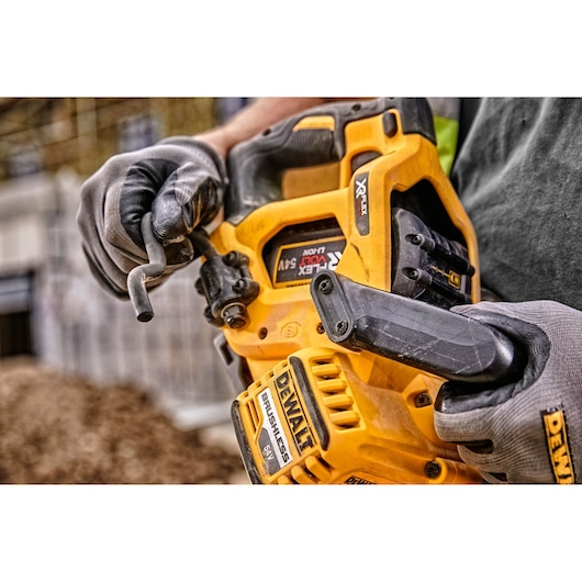 A close-up of a person wearing gloves holding a DEWALT cordless power tool with a yellow casing, adjusting a component on