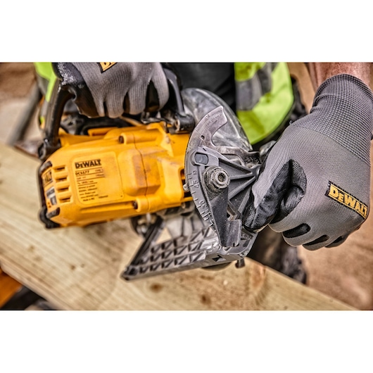 Close-up of a person wearing DEWALT branded gloves adjusting the angle setting on a DEWALT DCS577T2 circular saw while