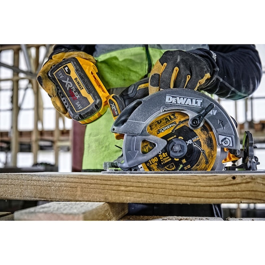 Worker uses DEWALT cordless circular saw to cut wood. The saw has a yellow XR FLEXVOLT battery attached.