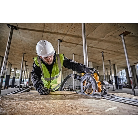 A construction worker wearing a white hard hat, safety gloves, and a high-visibility vest is operating a DEWALT DCS579T2