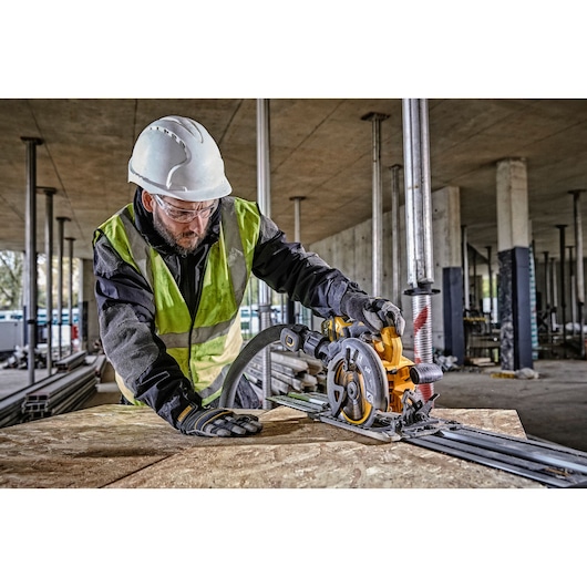A person wearing safety gear, including a helmet, gloves, and a high-visibility vest, is using a DEWALT circular saw to cut