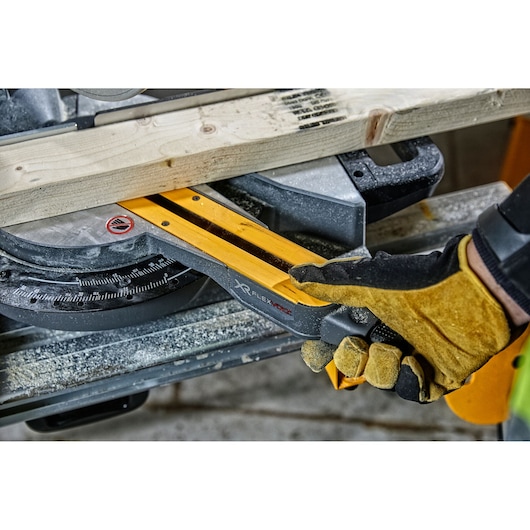 Close-up of a gloved hand operating a DEWALT XR FLEXVOLT miter saw to cut a wooden plank, with sawdust visible on the tool.