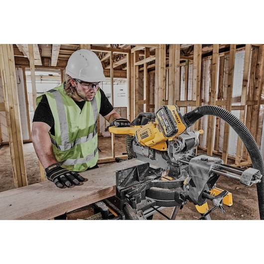 Worker uses DEWALT DCS781N saw to cut wood at a construction site. Safety gear and reflective vest worn.
