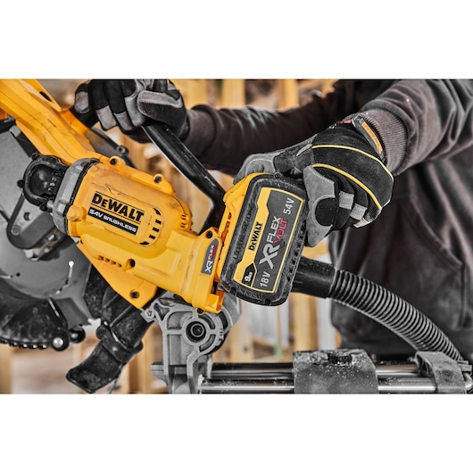 Person installs DEWALT XR FLEXVOLT battery on a yellow brushless saw at a construction site.