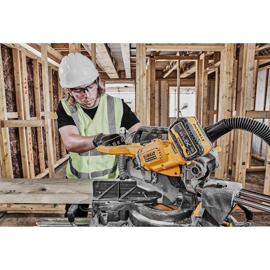 DEWALT DCS781X2-QW, DCS781X2 saw used in construction. Worker in safety gear operates miter saw on wood.