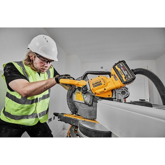 DEWALT DCS781X2-QW, DCS781X2 saw in use at jobsite. Worker with helmet and vest operates the saw indoors.