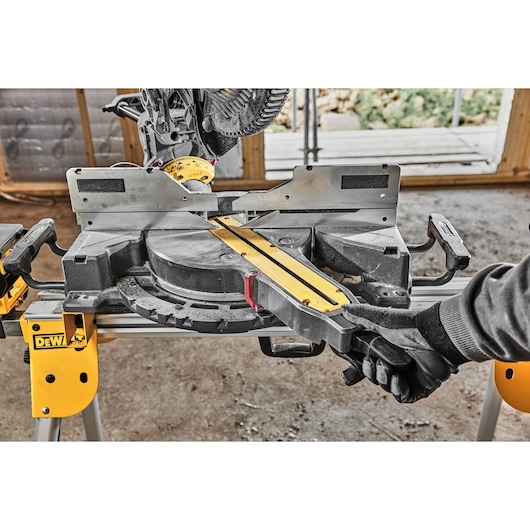 DEWALT miter saw in workshop. Models DCS781X2-QW, DCS781X2 shown. Gloved hand adjusts the saw.