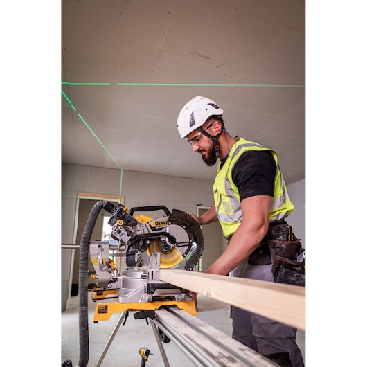 Worker using DEWALT DCS782N saw to cut wood indoors; safety gear and laser guides are visible.