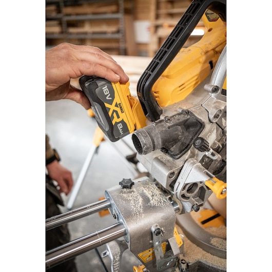 Hand inserting battery into DEWALT DCS782N saw in workshop with wood dust on tool.