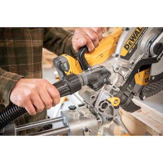 Person connects vacuum hose to DEWALT miter saw for dust extraction in woodworking.
