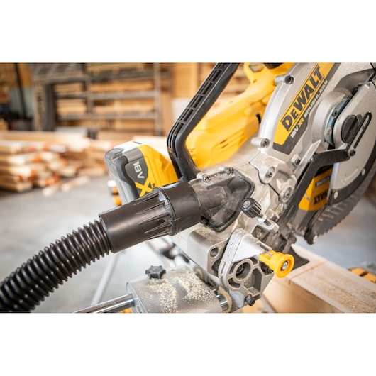Close-up of a DEWALT cordless mitre saw with dust extraction hose attached, in a wood workshop.