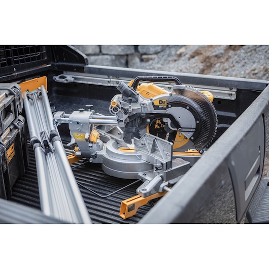 DEWALT miter saw DCS782N placed in a truck bed, surrounded by toolboxes and metal rods.